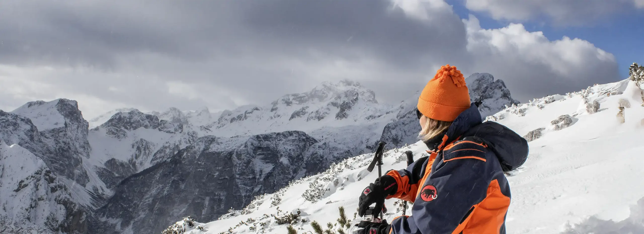 Hiker sitting on a snowy alpine ridge overlooking Mount Triglav in the Julian Alps, Slovenia, during winter day.